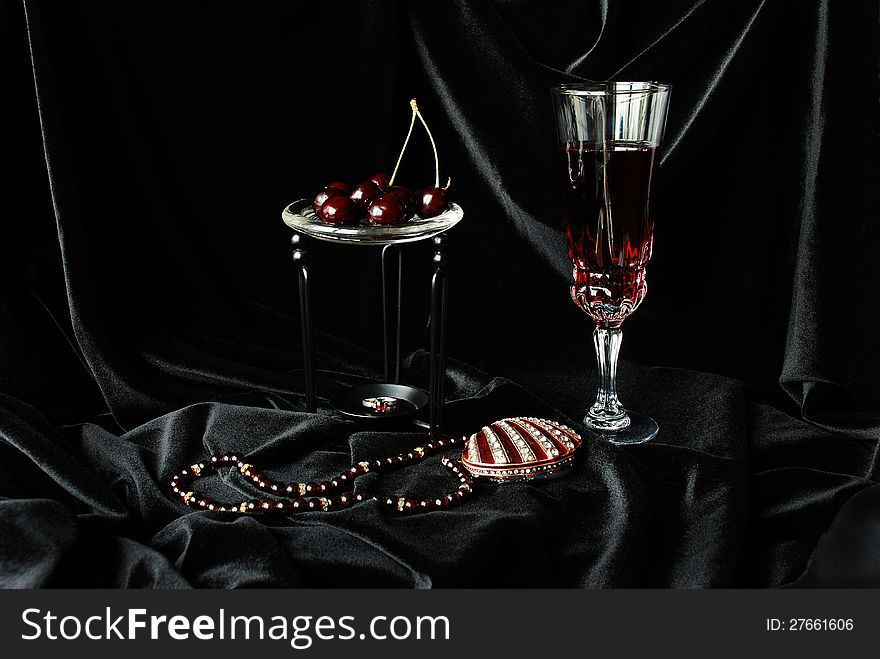 Glass of wine, a garnet necklace, black cherry and a jewelry box on black velvet. Glass of wine, a garnet necklace, black cherry and a jewelry box on black velvet