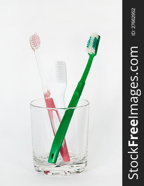 Three toothbrushes in a glass beaker on a white background