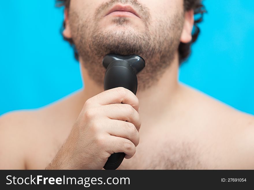 The man holds in a hand the electric razor at a chin, a half of the face. The man holds in a hand the electric razor at a chin, a half of the face