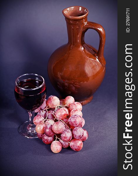Glass and a jug of red wine on a dark background