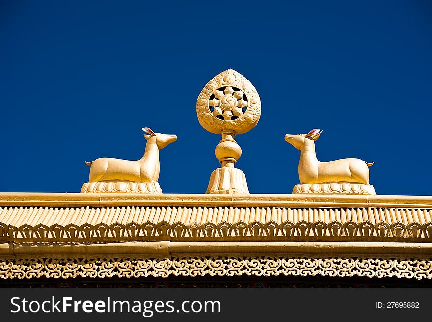 Tibetan Monastery Gates. Buddhist symbols: Dharma-wheel and deer on decorated roof under blue sky at Thiksey Gompa. India, Ladakh, Thiksey Monastery