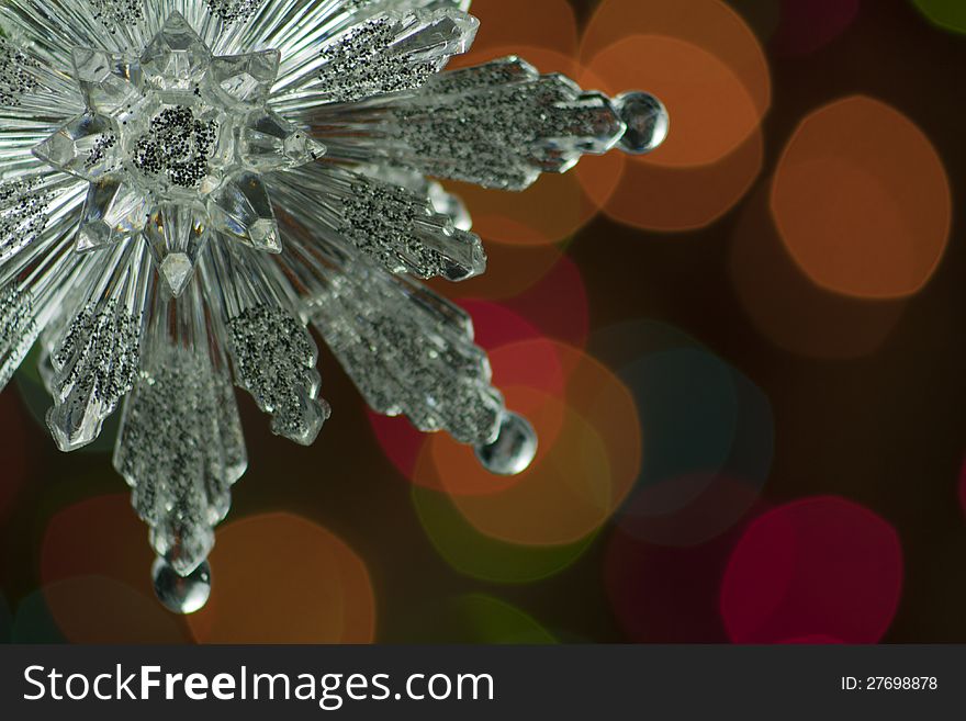 Silver snowflake Christmas ornament suspended from a pine bough against bokeh effect background