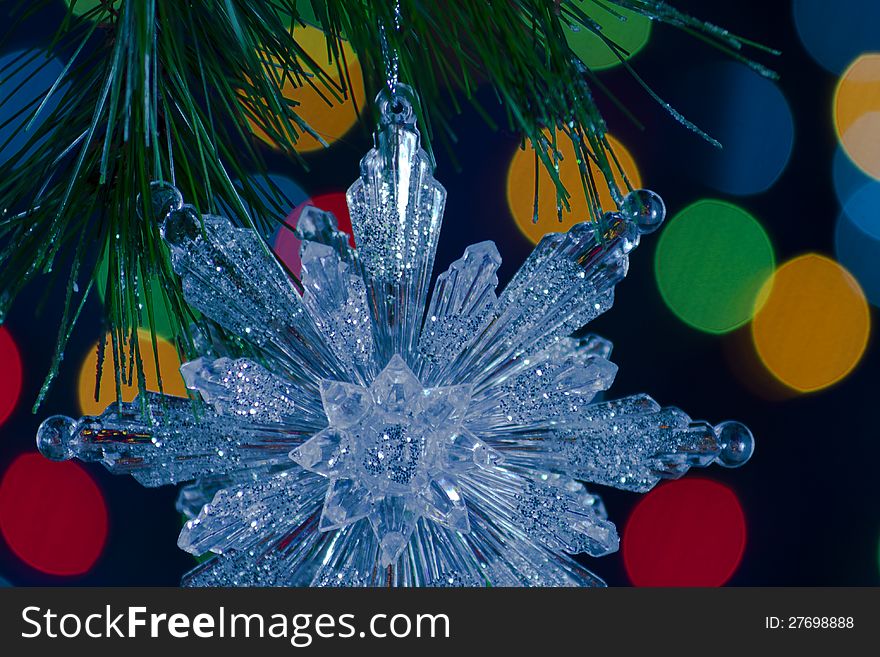 Snowflake Christmas ornament suspended from a pine bough against bokeh light background. Snowflake Christmas ornament suspended from a pine bough against bokeh light background