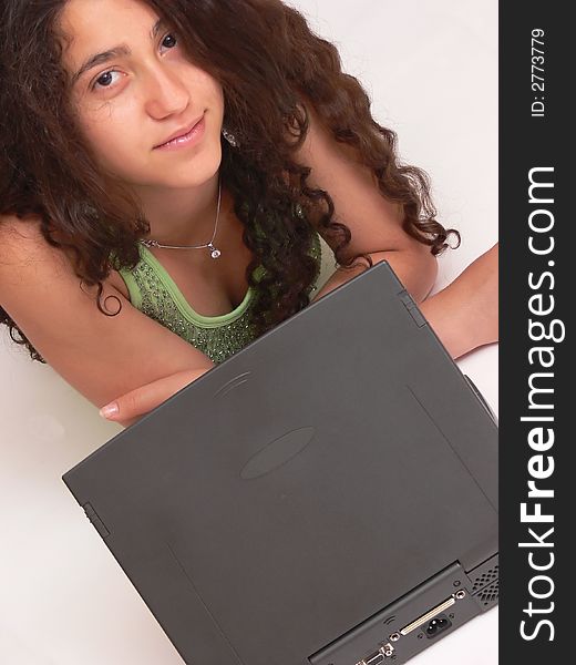 A young girl laying on the floor with her nice long curly dark hair working on the laptop and looks up to the camera. On white background. A young girl laying on the floor with her nice long curly dark hair working on the laptop and looks up to the camera. On white background.