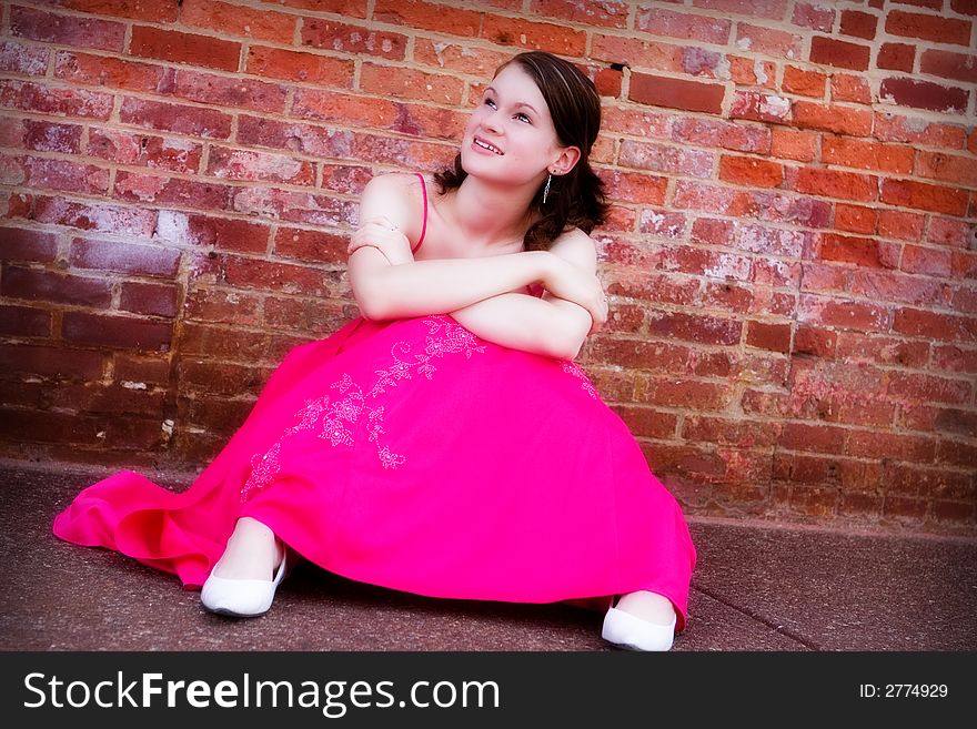 Beautiful, smiling teen in formal wear gazing up from the sidewalk by an old brick wall. Beautiful, smiling teen in formal wear gazing up from the sidewalk by an old brick wall.