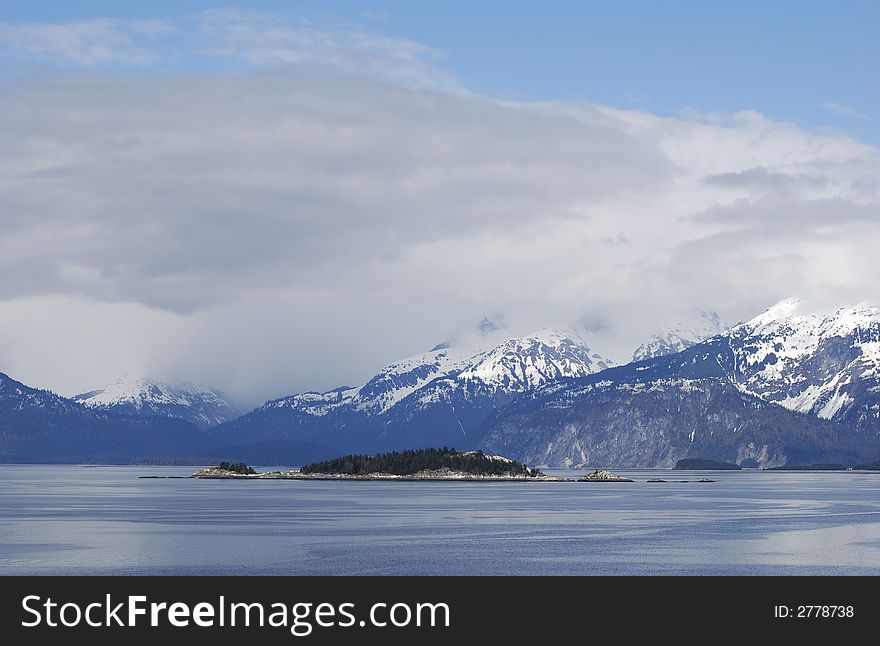 The lonely island with snowy mountains in a background (Inside Passage, Alaska).