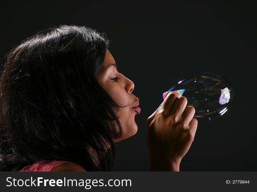 Portrait of attractive teenager blowing bubbles against black background