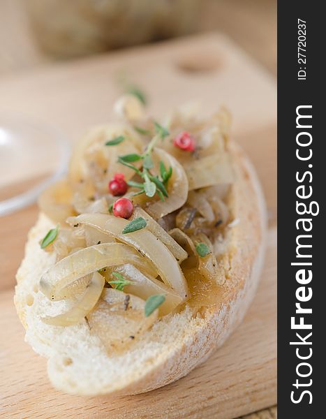 Confit of caramelized onions with thyme and pepper on a piece of baguette on a wooden board closeup vertical, selective focus. Confit of caramelized onions with thyme and pepper on a piece of baguette on a wooden board closeup vertical, selective focus