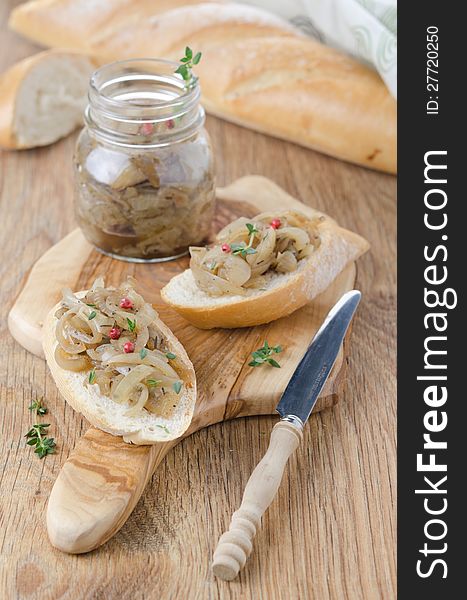 Confit of caramelized onions with thyme and pepper on a piece of baguette on a wooden board. Confit of caramelized onions with thyme and pepper on a piece of baguette on a wooden board