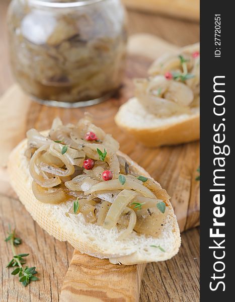 Confit of caramelized onions with thyme and pepper on a piece of baguette on a wooden board closeup. Confit of caramelized onions with thyme and pepper on a piece of baguette on a wooden board closeup