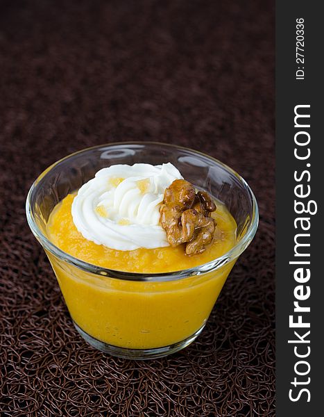 Dessert of mango and pumpkin in a glass beaker decorated with whipped cream and caramelized walnuts on a dark background. Dessert of mango and pumpkin in a glass beaker decorated with whipped cream and caramelized walnuts on a dark background