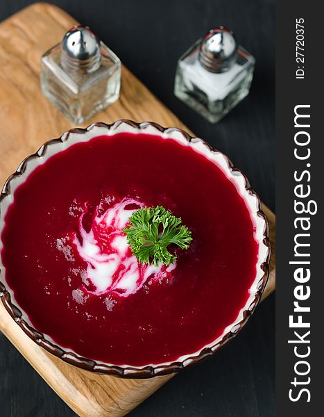 A bowl of tomato soup with beetroot, yoghurt and decorated with greens on a wooden board, top view. A bowl of tomato soup with beetroot, yoghurt and decorated with greens on a wooden board, top view