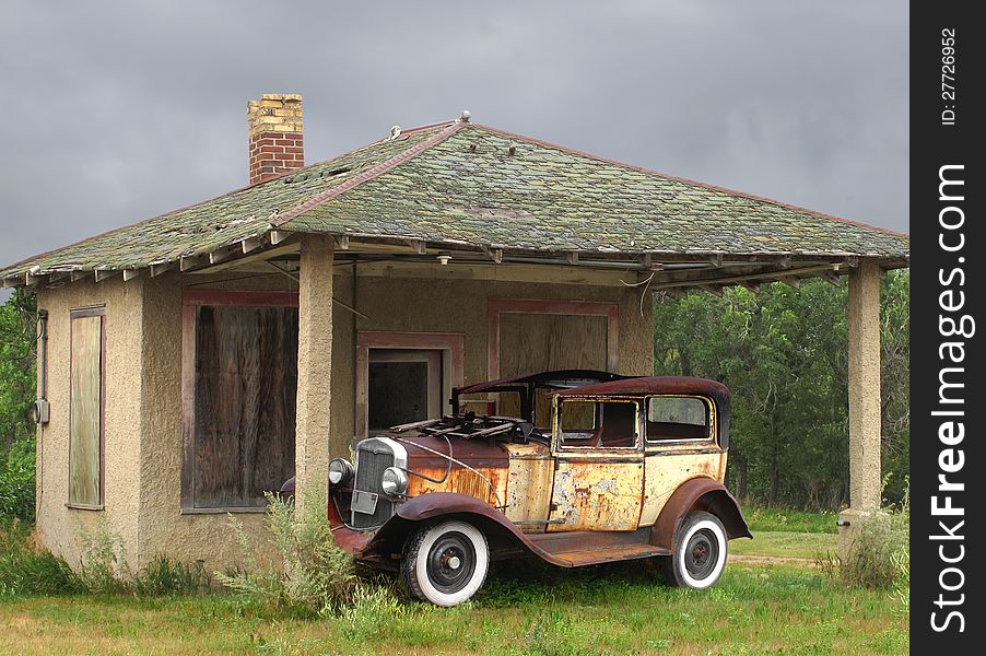 Old rusted, weathered, and wrecked car, sitting on the grass under the awning of a small building in a rural area. Old rusted, weathered, and wrecked car, sitting on the grass under the awning of a small building in a rural area.