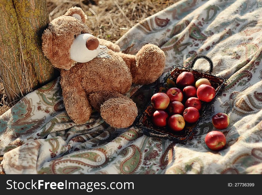 Under a tree on a blanket sitting bear with red apples. Under a tree on a blanket sitting bear with red apples