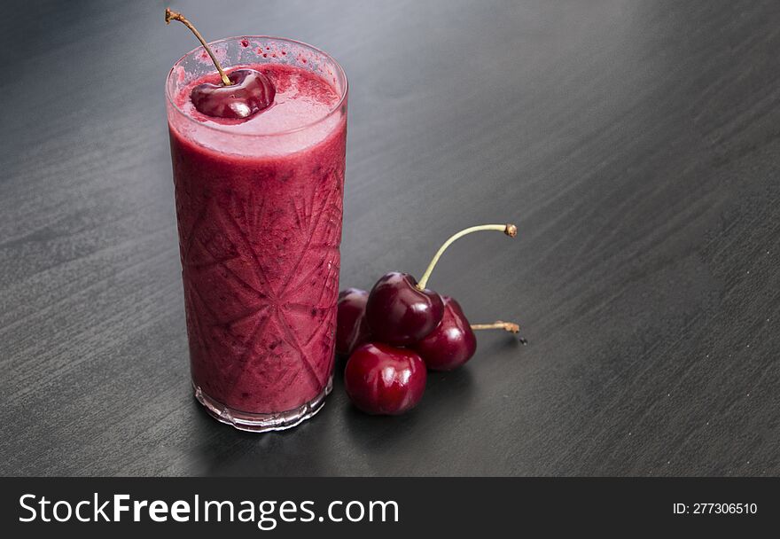 a glass of smoothie made with fresh cherries on dark background