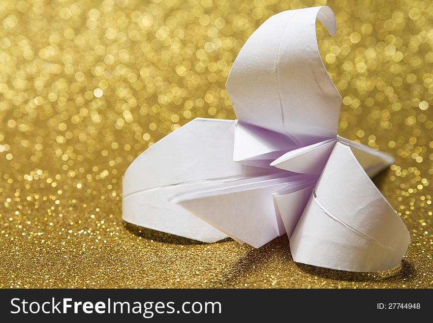 White paper origami lily on golden glitter background