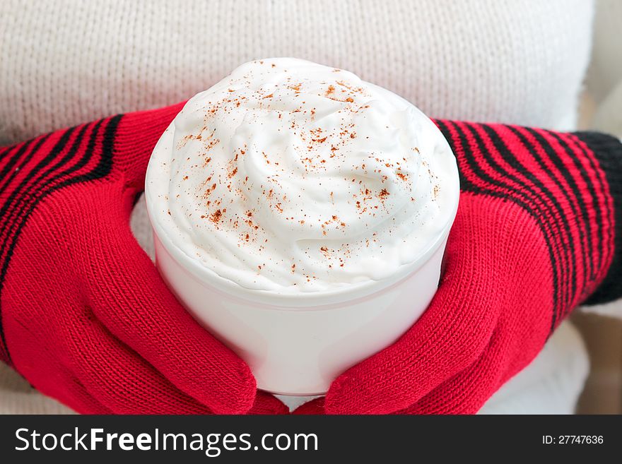 Seasonal drink topped with whipped cream and cinnamon held by person wearing red wool gloves. Seasonal drink topped with whipped cream and cinnamon held by person wearing red wool gloves