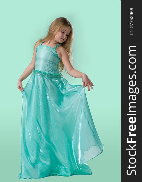 Full-length portrait of cute little girl in a smart long silk dress playfully posing in studio on light green background. Full-length portrait of cute little girl in a smart long silk dress playfully posing in studio on light green background