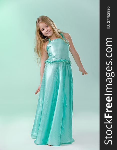 Full-length portrait of cute little girl in a smart long silk dress playfully posing in studio on light green background. Full-length portrait of cute little girl in a smart long silk dress playfully posing in studio on light green background