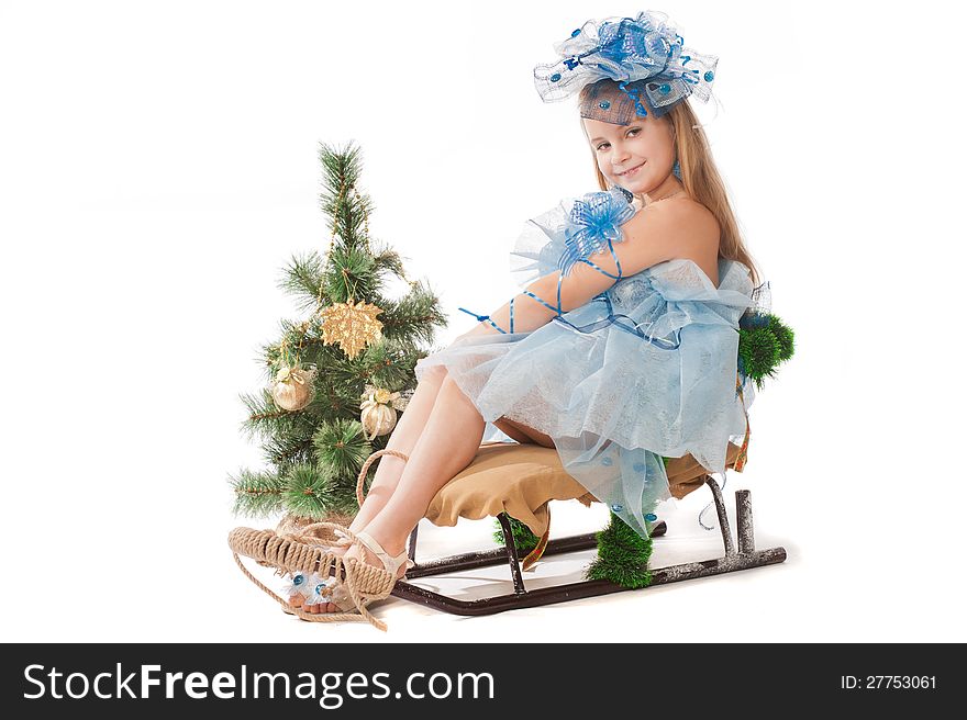 Portrait of a cute little girl in a beautiful dress and ornaments for the head against the Christmas tree and a sledge. Portrait of a cute little girl in a beautiful dress and ornaments for the head against the Christmas tree and a sledge