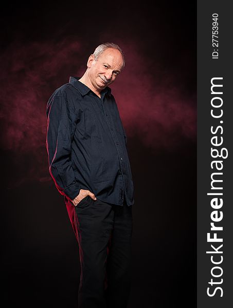 Elderly man in a black shirt standing on a dark background