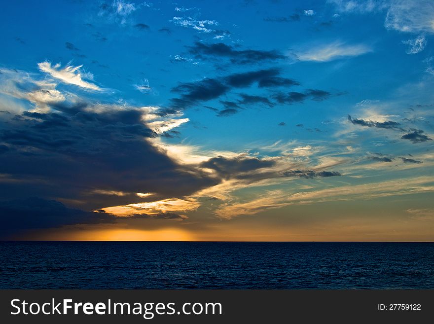 A beautiful panorama of a sunset on a calm sea, with a dark cloud on blue sky.