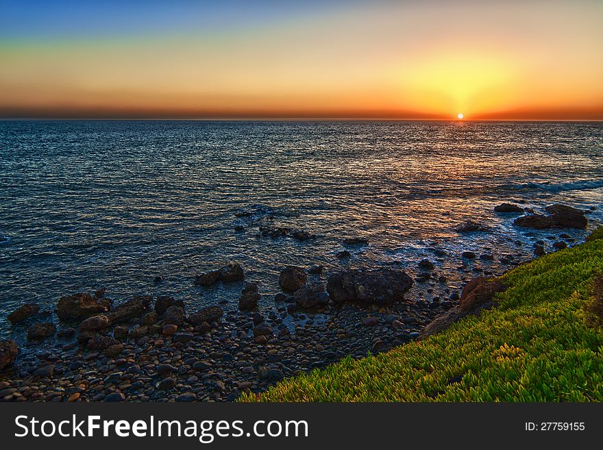 Sunset on a calm sea with a green grass and rocks