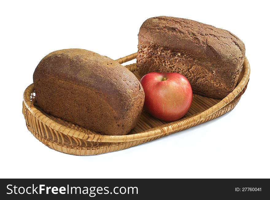 Two loaves of rye bread and an apple in a straw basket. Two loaves of rye bread and an apple in a straw basket