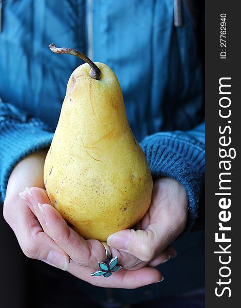 Woman hands holding a big pear on a dark blue green background and a flower ring. Woman hands holding a big pear on a dark blue green background and a flower ring