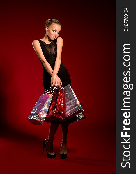 Sexy girl in a black dress with bags in hands on a dark red background