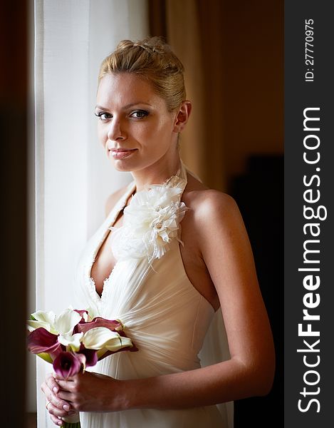 Happy bride with bouquet of calla near sunny window