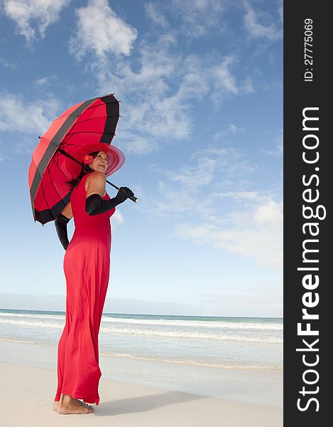 Beautiful looking lady posing happy smiling in elegant red dress, black gloves and umbrella at beach,  with ocean and blue sky as background and copy space. Beautiful looking lady posing happy smiling in elegant red dress, black gloves and umbrella at beach,  with ocean and blue sky as background and copy space.