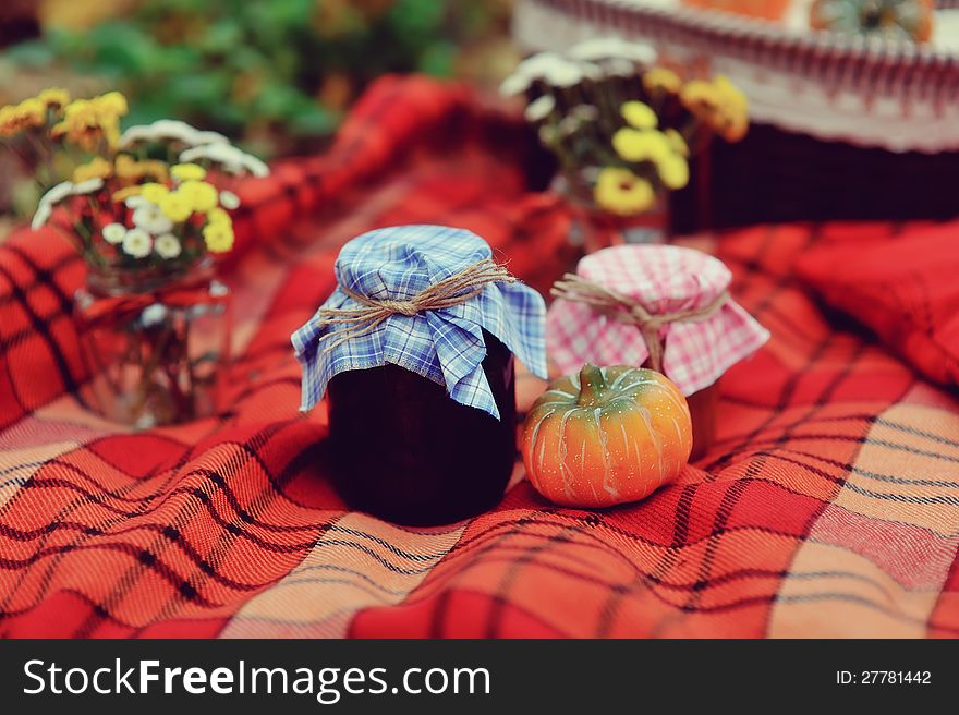 Banks on the red tablecloth with jam, pumpkins and autumn flowers bouquets. Banks on the red tablecloth with jam, pumpkins and autumn flowers bouquets