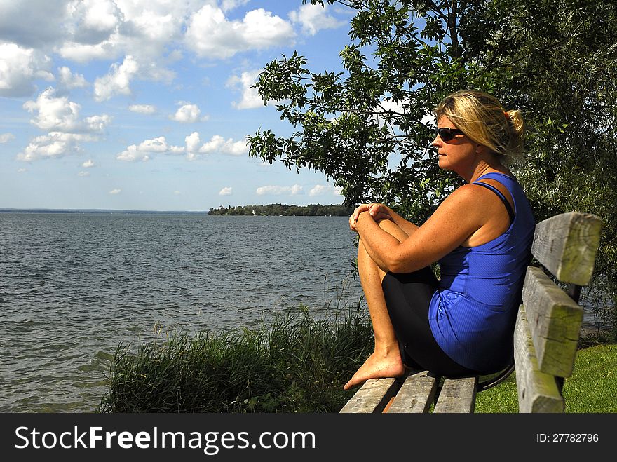 A woman sits on a bench by the water, contemplating. A woman sits on a bench by the water, contemplating.