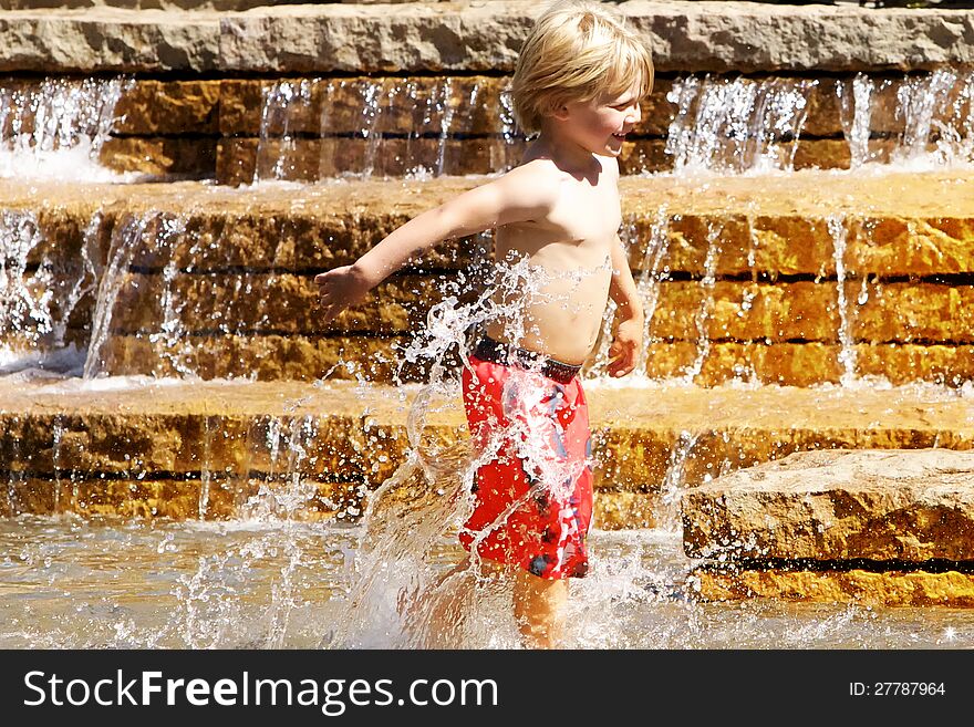 Little boy in red swimtrucks splashing in water fountain. Little boy in red swimtrucks splashing in water fountain