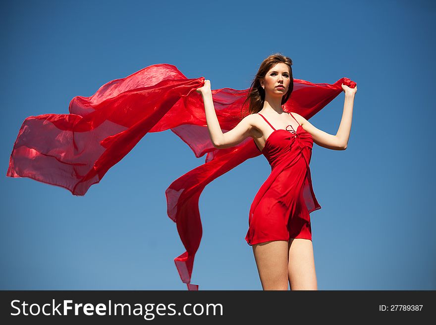 The girl in a red dress with fluttering silk against the blue sky. The girl in a red dress with fluttering silk against the blue sky