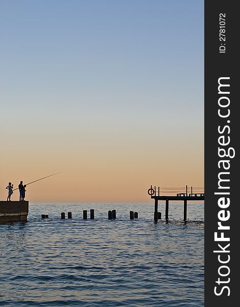 Sundown on sea. Three fisherman on pier