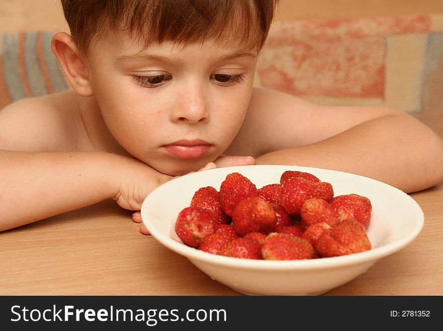 The child looks at a plate with red berries