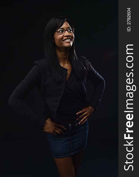 African America woman wearing glasses, black jacket and top with a denim mini skirt.  She is smiling with her hands on her hips. African America woman wearing glasses, black jacket and top with a denim mini skirt.  She is smiling with her hands on her hips.