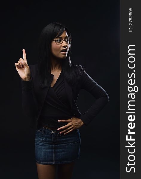 African America woman wearing glasses, black jacket and top with a denim mini skirt. She has her right hand and indew finger pointed to sky and a surprised expression on her face. African America woman wearing glasses, black jacket and top with a denim mini skirt. She has her right hand and indew finger pointed to sky and a surprised expression on her face.