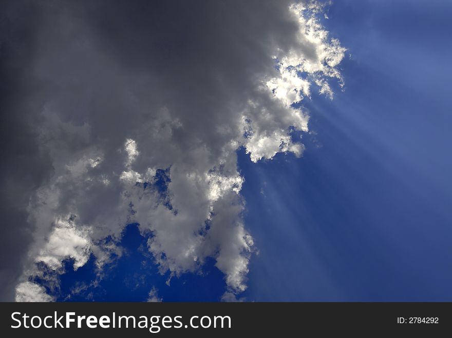 View of white and gray storm clouds in blue sky with rays of light. View of white and gray storm clouds in blue sky with rays of light