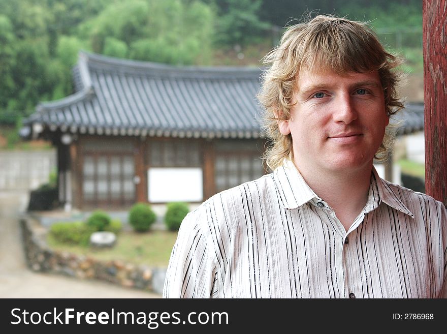 Blond man smiling with oriental buildings in the background - travel and tourism. NOTE: Light rain, not noise.