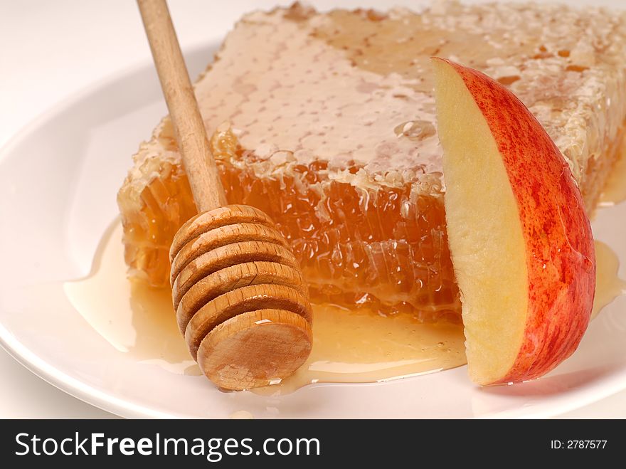 A honeycomb and honey wand on a white plate with an apple slice. A honeycomb and honey wand on a white plate with an apple slice