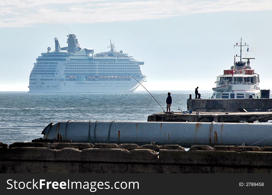 A modern cruise ship is sailling away from Lisbon. At the right of the picture is a small ferry, and some fishermen. A modern cruise ship is sailling away from Lisbon. At the right of the picture is a small ferry, and some fishermen.