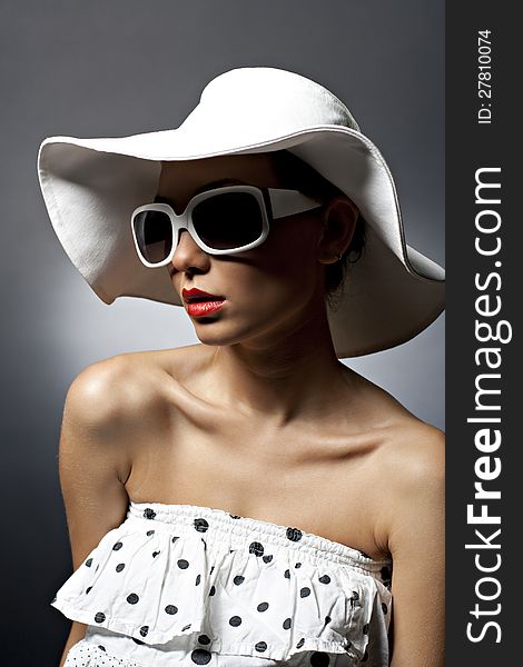 Portrait of beautiful young woman with dark sunglasses and white hat. Red lipstick. Wearing white shirt with black dots. Portrait of beautiful young woman with dark sunglasses and white hat. Red lipstick. Wearing white shirt with black dots.