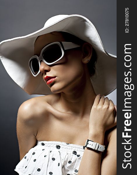 Portrait of beautiful young woman with sunglasses, white hat and white dress with black dots. Red lipstick. Portrait of beautiful young woman with sunglasses, white hat and white dress with black dots. Red lipstick