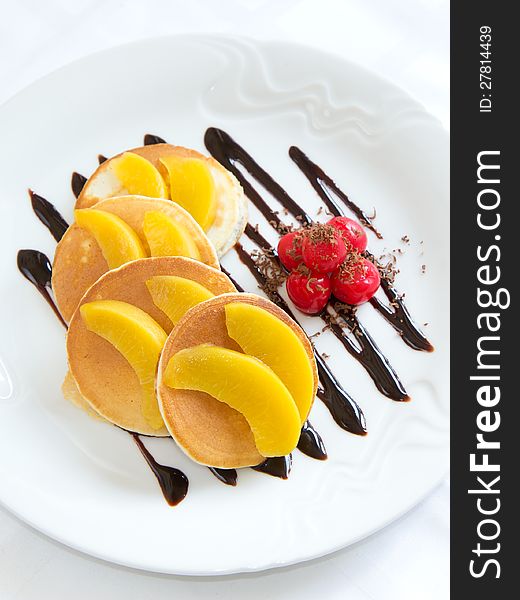 Delicious pancakes with pieces of peach, cherry and chocolate syrup.