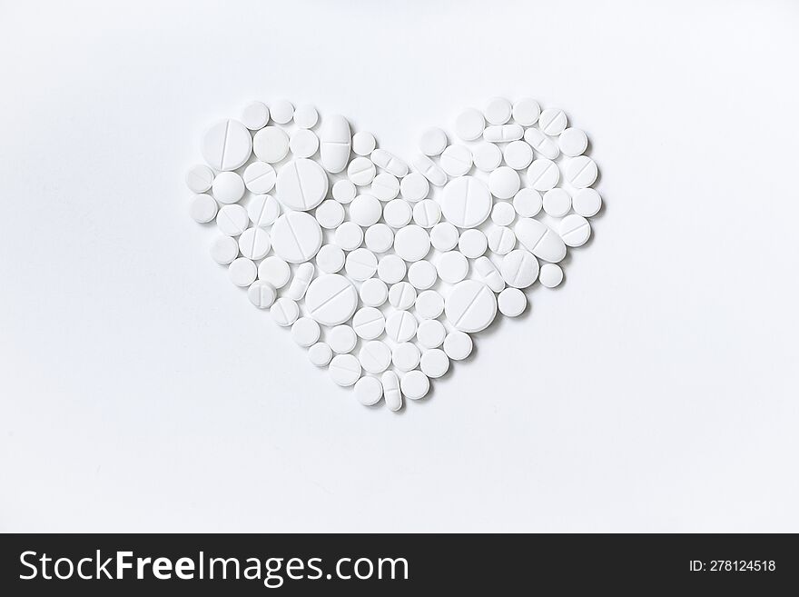 A heart made of tablets of different sizes. White medicines, different shapes, white background.