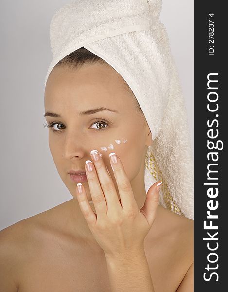 Beautiful woman in a white towel applying moisturizer cream on face. Beautiful woman in a white towel applying moisturizer cream on face.