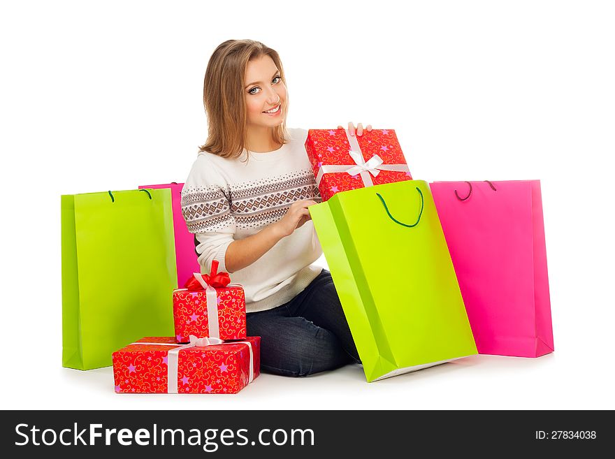 Young beautiful blond woman in white jumper with ornament and jeans puts gift in shopping bags, sits isolated on white. Young beautiful blond woman in white jumper with ornament and jeans puts gift in shopping bags, sits isolated on white